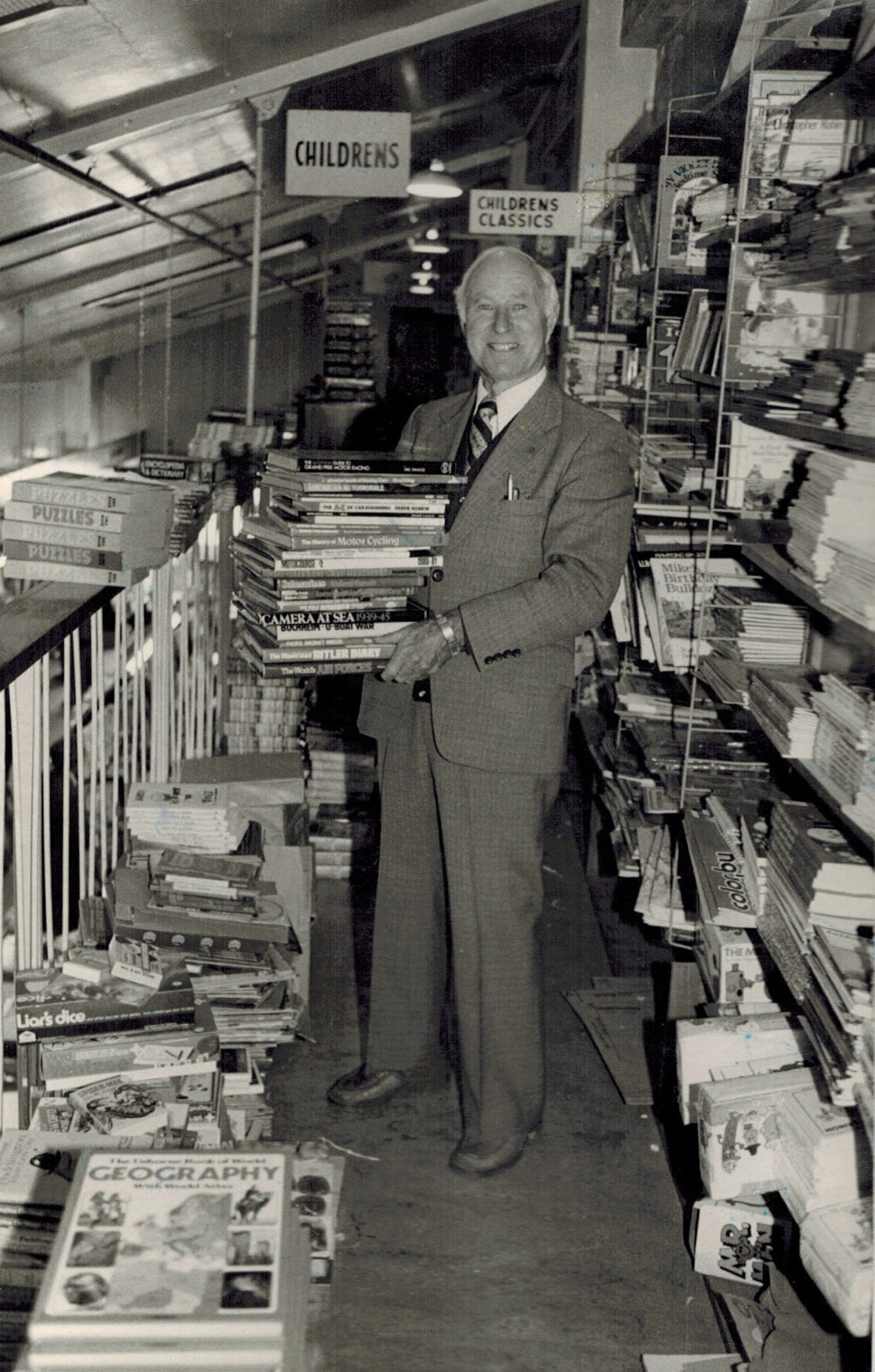 Second generation Alex Hedley dressed in a suit and holding a stack of books upstairs at 150 Queen St Masterton