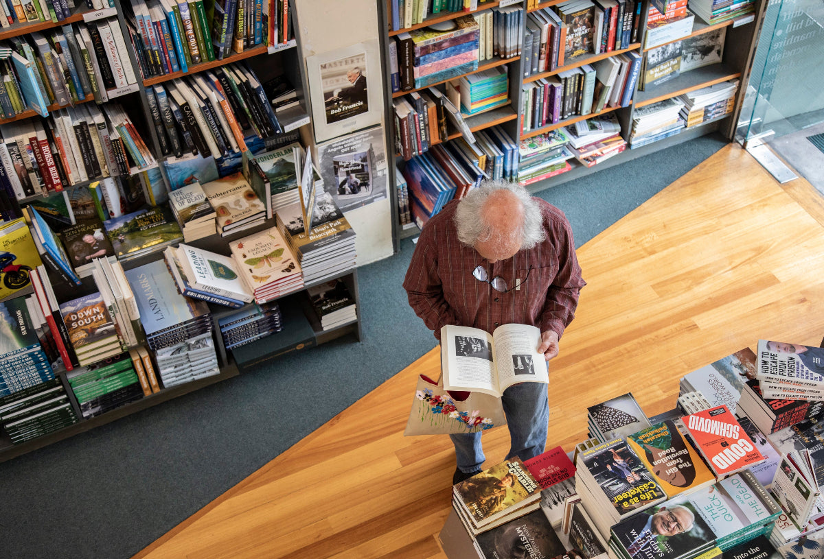 Man reading a book in Hedley's Books in Masterton with shelves filled with books.